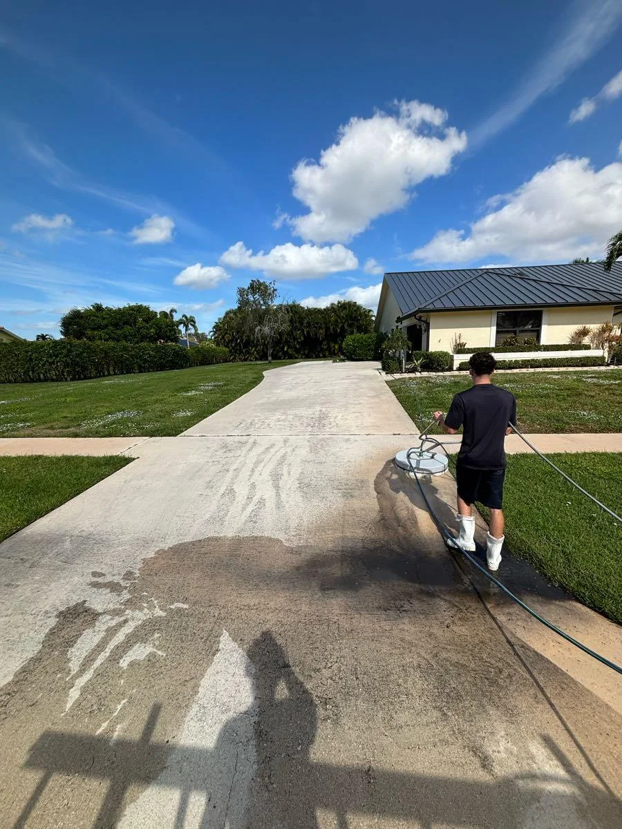 A driveway caught mid-wash: the near side still dark with grime, the far side already bright